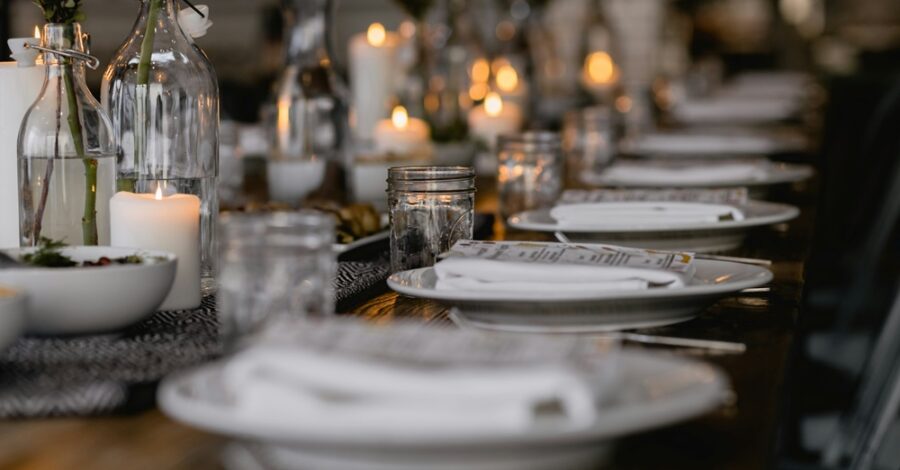 A table set for a dinner party with white plates, cutlery and glass jars.
