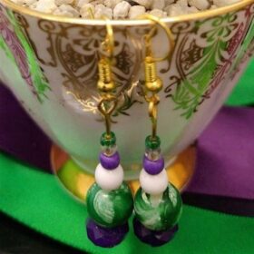 A pair of purple, white and green earrings hanging on the rim of a china teacup