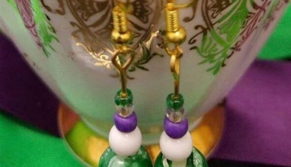 A pair of purple, white and green earrings hanging on the rim of a china teacup