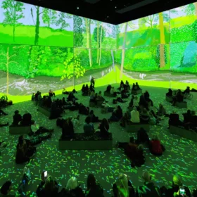 A group of adults sat on beanbags in Aviva Studios gallery space with a large-scale projection of artist David Hockney's work.