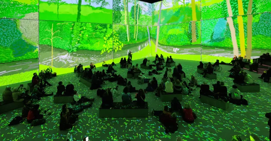 A group of adults sat on beanbags in Aviva Studios gallery space with a large-scale projection of artist David Hockney's work.