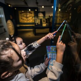 Two young visitors looking up at a banner in a case, holding pencils and an activity sheet.