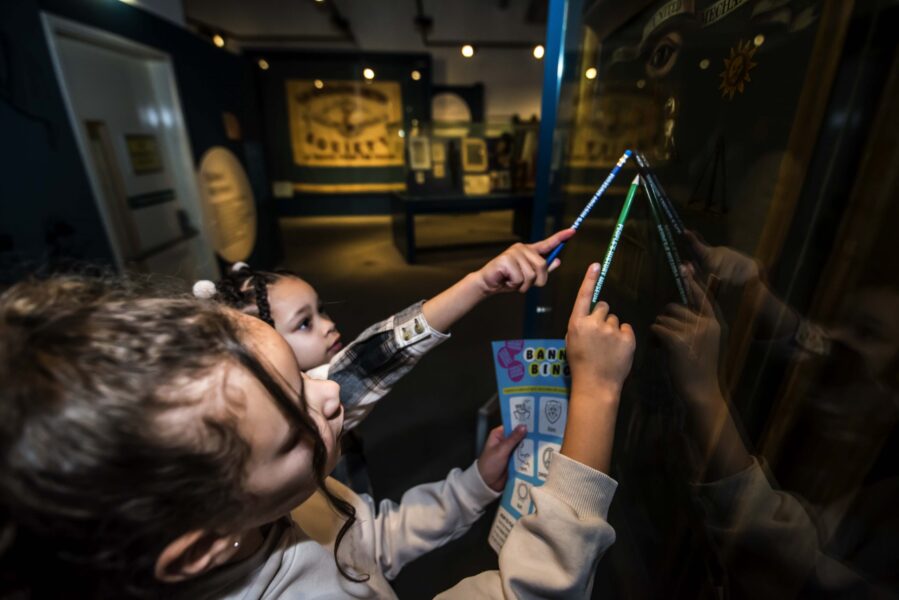 Two young visitors looking up at a banner in a case, holding pencils and an activity sheet.