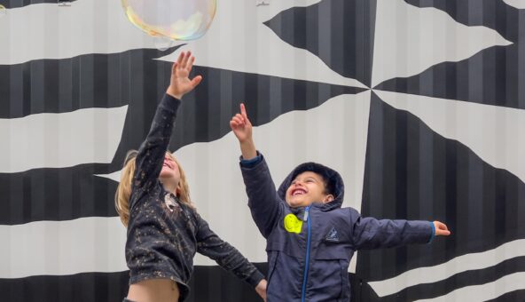 Two small children reaching up to touch a huge bubble.