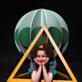 Image of actor within the set, wearing green pom poms.