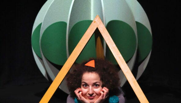 Image of actor within the set, wearing green pom poms.