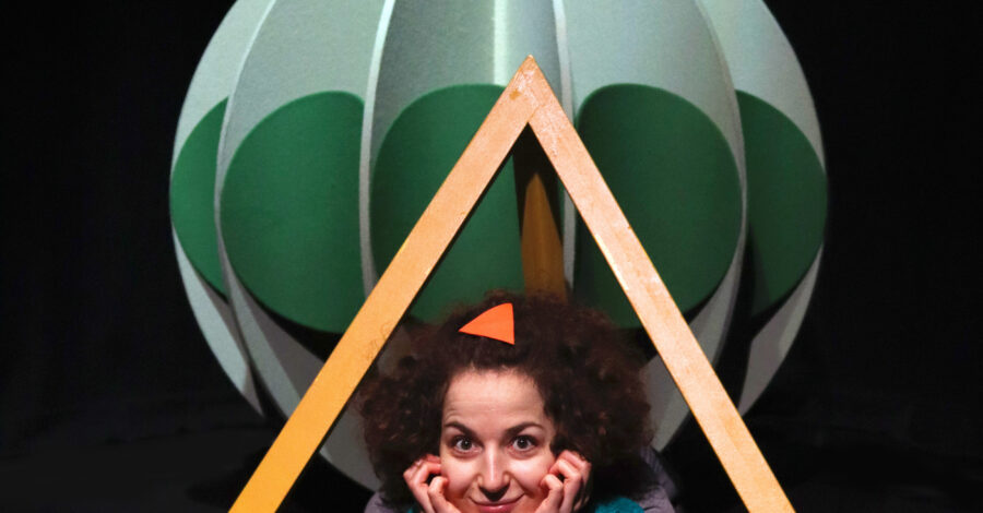 Image of actor within the set, wearing green pom poms.