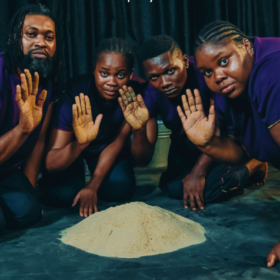 Four people resting on their knees, gathered around a pile of sand with their right hands in the air.