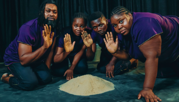 Four people resting on their knees, gathered around a pile of sand with their right hands in the air.