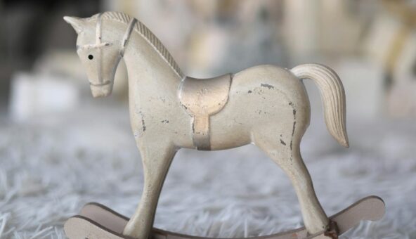 A small white wooden rocking horse with a gold saddle. The toy is placed on a fluffy grey carpet.