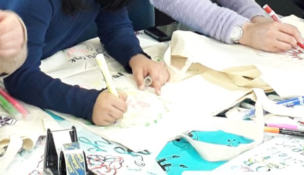 A close-up of a pair of hands decorating a tote bag.