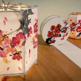 Three white Chinese paper lanterns with pink, green and red painted designs on them.