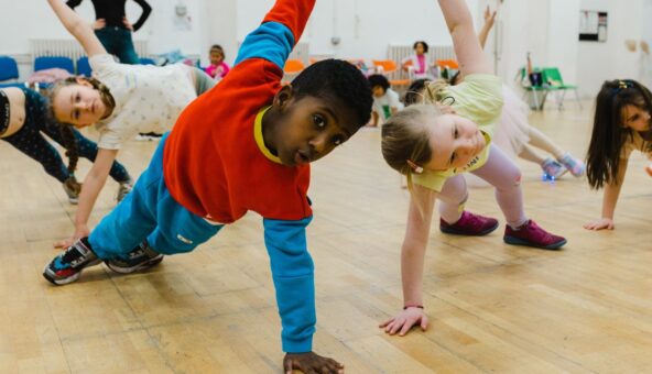 Two young children pose with two feet and one hand on the floor while the other arm is extended towards the ceiling in a studio.