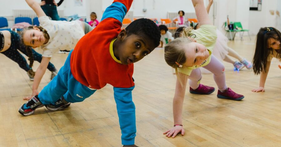 Two young children pose with two feet and one hand on the floor while the other arm is extended towards the ceiling in a studio.