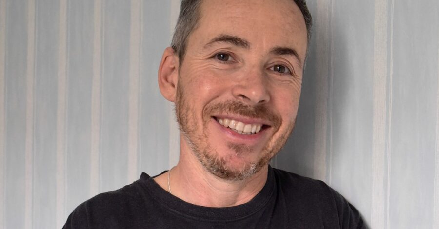 A photograph of Jay Prosser. A middle-aged man with short dark hair and brown eyes. He is smiling. He's got a short-trimmed beard and is wearing a black T-shirt.