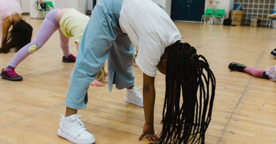 A yoga class in a studio with a light wooden floor. Several people are in the downward dog yoga position.