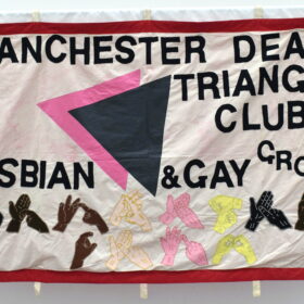 A textile banner featuring text: 'Manchester Deaf Triangle Club, Lesbian & Gay Group', and different coloured hands doing sign language.