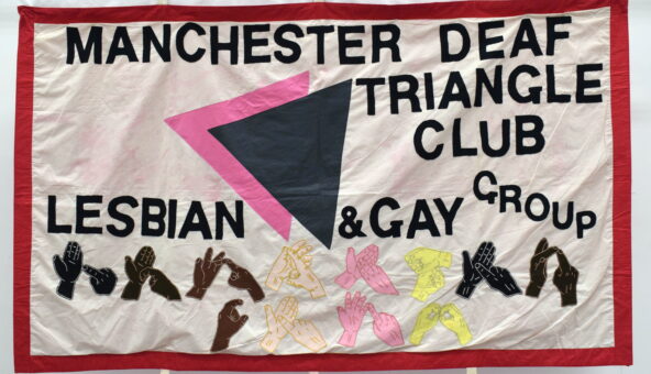 A textile banner featuring text: 'Manchester Deaf Triangle Club, Lesbian & Gay Group', and different coloured hands doing sign language.