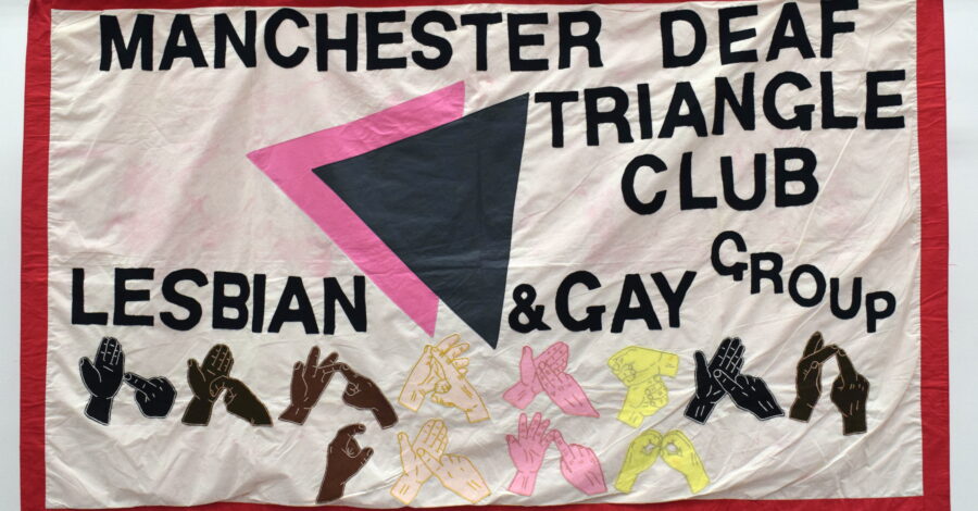 A textile banner featuring text: 'Manchester Deaf Triangle Club, Lesbian & Gay Group', and different coloured hands doing sign language.