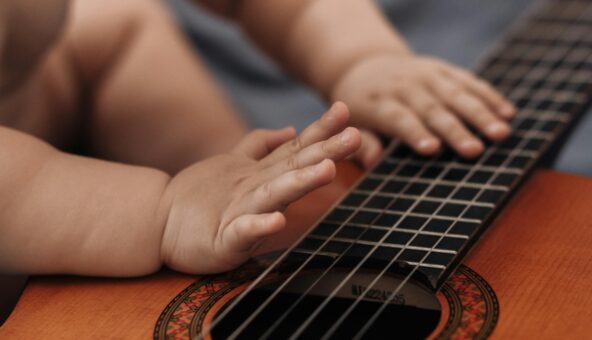 A toddler's hands tapping on the strings of an acoustic guitar