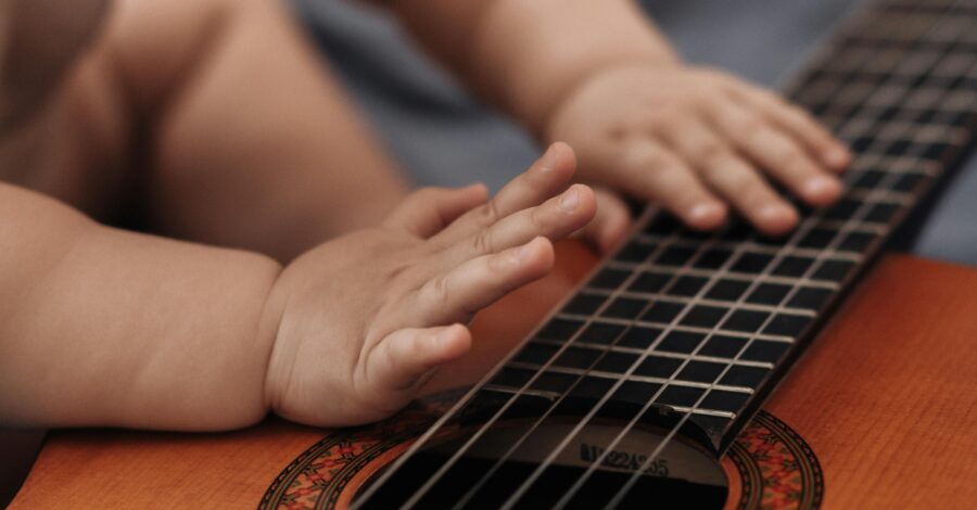 A toddler's hands tapping on the strings of an acoustic guitar