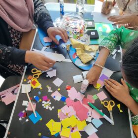 Birds eye view of a table filled with coloured paper, pens and scissors where children are crafting.