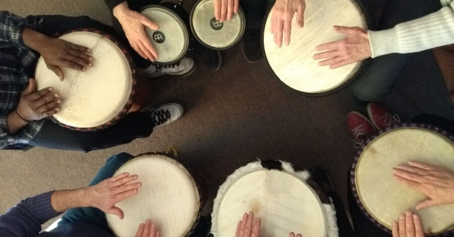 Image from above of 6 pairs of hands playing small drums