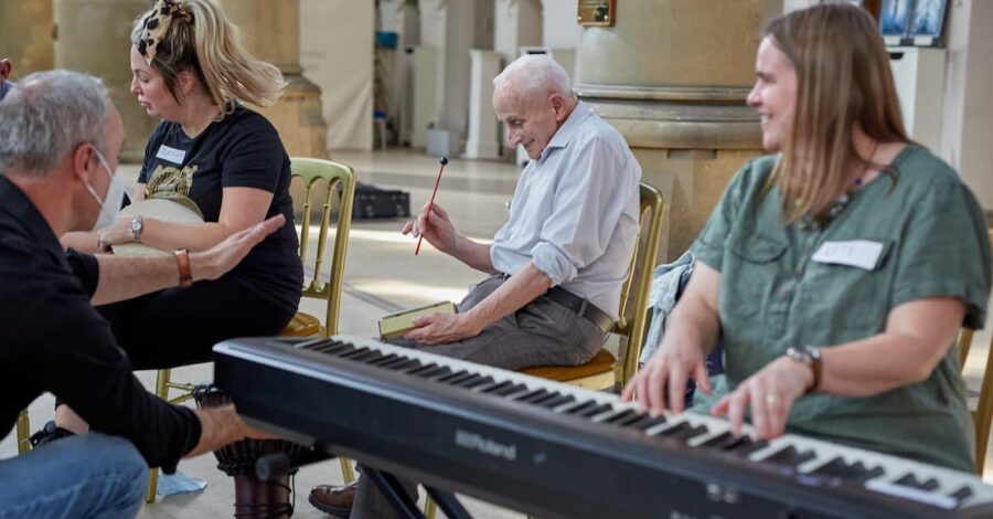 Woman in a green top playing a piano. In the background an older man playing rhythm