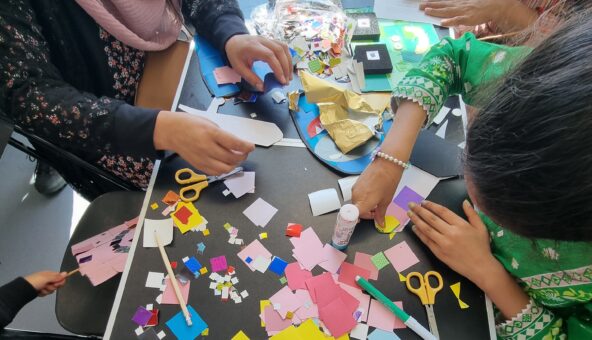 A table filled with coloured paper, pens and scissors where children are crafting.