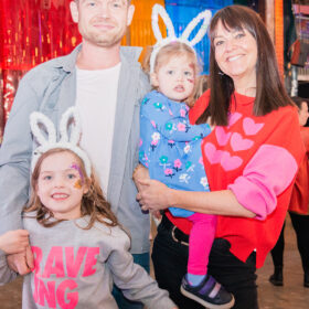 A family consisting of a father, mother and two young children, wearing bunny ear headbands, smiling.