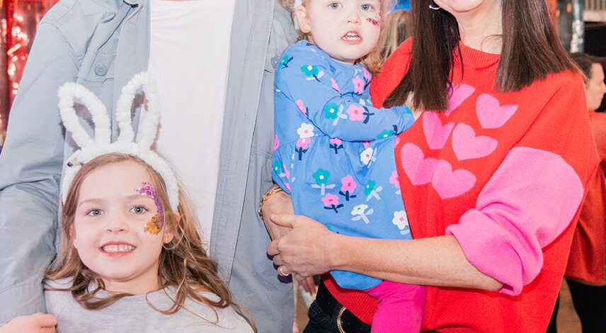 A family consisting of a father, mother and two young children, wearing bunny ear headbands, smiling.