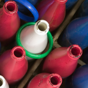 A ring toss game consisting of red, blue and white milk bottles. A green hoop has landed around one of the white bottles.