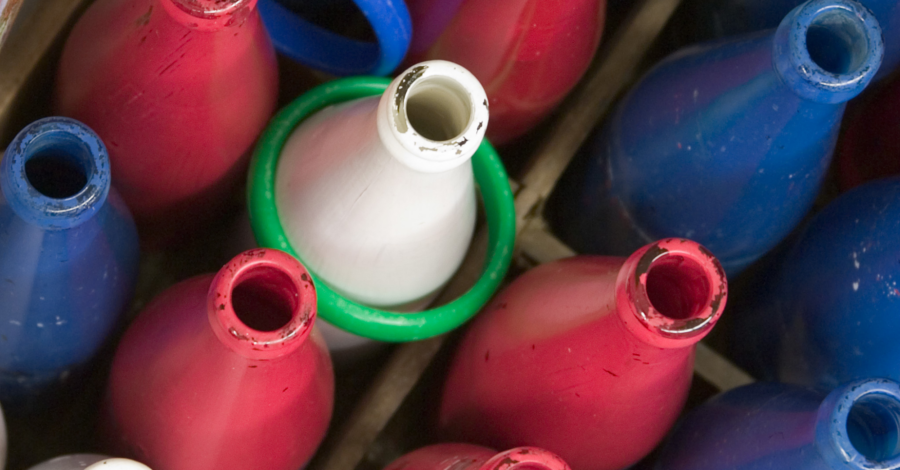 A ring toss game consisting of red, blue and white milk bottles. A green hoop has landed around one of the white bottles.