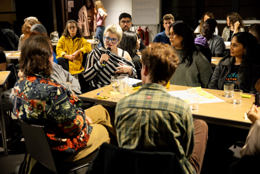Someone speaking into a microphone sat at a table surrounded by others who are listening.