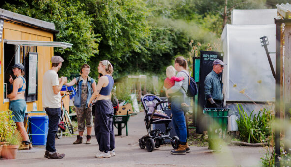A group of people dressed in light summer clothing stood outside on a tree-lined path.