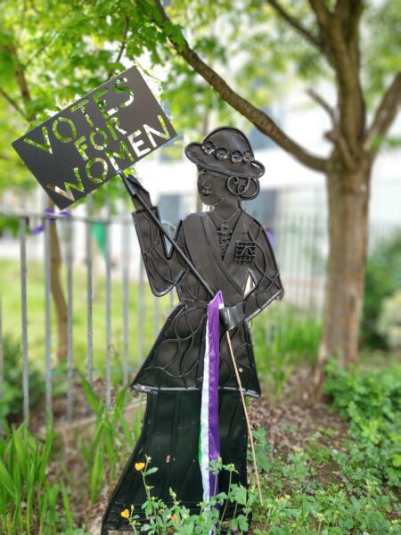 Metal Suffragette sculpture holding a 'Votes for Women' sign.