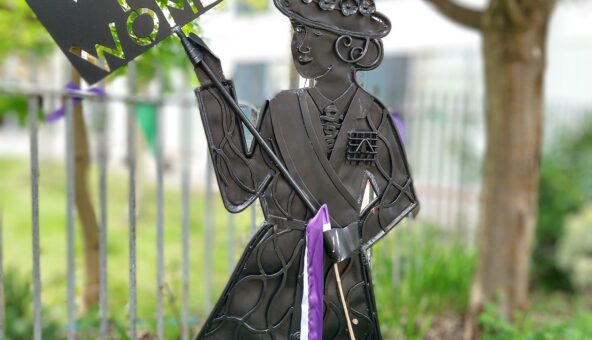 Metal Suffragette sculpture holding a 'Votes for Women' sign.