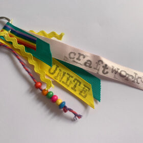 A set of ribbons on a keyring - one has coloured beads on it, another is printed with the word unite and another has the writing craftwork.
