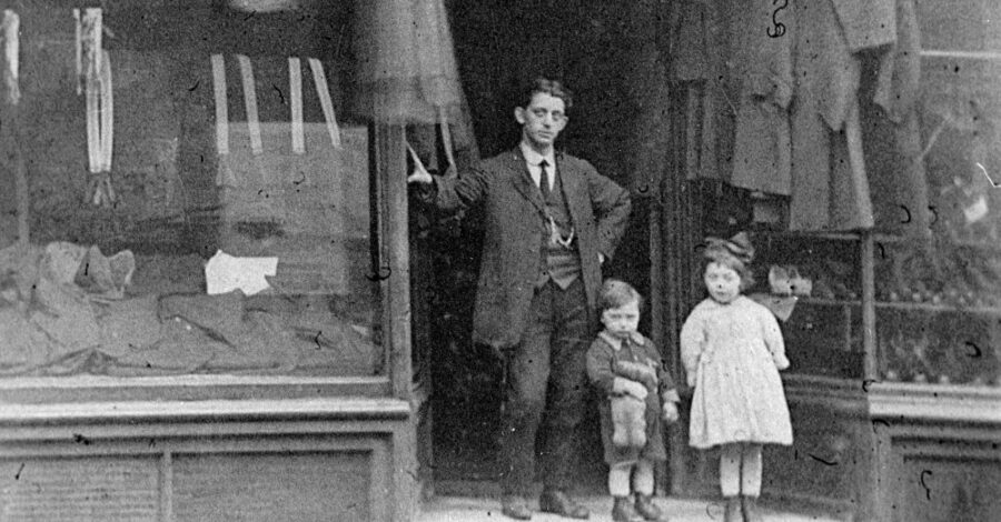 A black and white photograph showing an adult man and two young children standing in front of a clothing store.