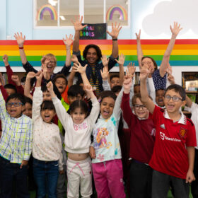 A group of childre standing facing the camera with both their hands up in the air.