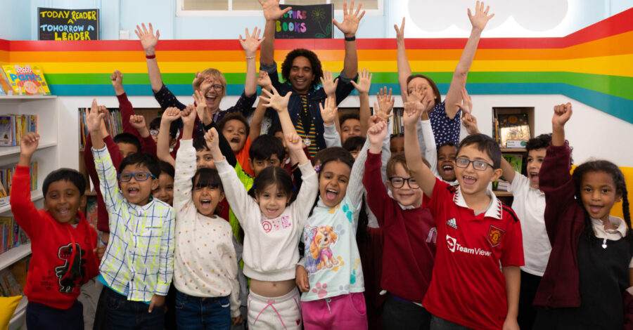 A group of childre standing facing the camera with both their hands up in the air.