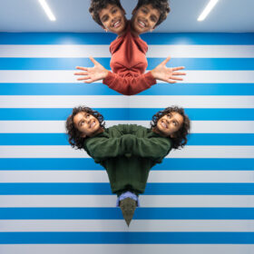 Inside the Symmetry Room at the Museum of Illusions. The walss are blue and white striped and two children are enjoying exploring the symmetry room. We can only see their heads and the top part of their bodies.