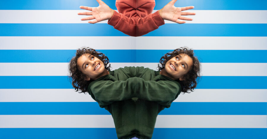 Inside the Symmetry Room at the Museum of Illusions. The walss are blue and white striped and two children are enjoying exploring the symmetry room. We can only see their heads and the top part of their bodies.