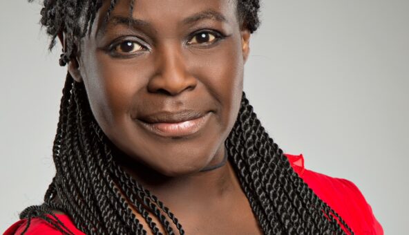 An image of Dame Maggie Aderin-Pocock, a black middle-aged woman with long hair in a red top, looking directly at the camera with a warm expression.