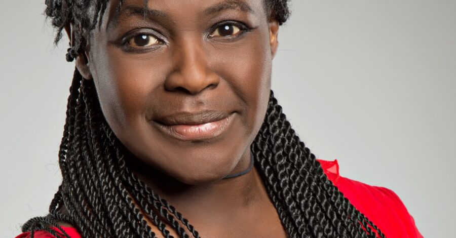 An image of Dame Maggie Aderin-Pocock, a black middle-aged woman with long hair in a red top, looking directly at the camera with a warm expression.