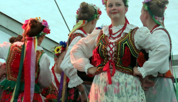 Four young female dancers in folk costumes, one looking at the camera