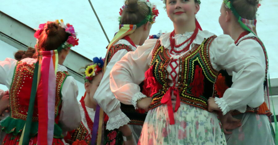 Four young female dancers in folk costumes, one looking at the camera