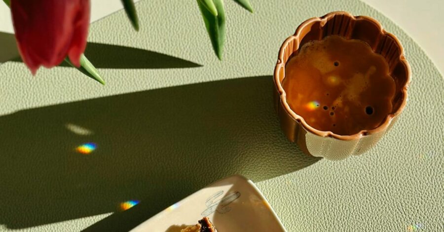 A cup of chai with a long shadow and piece of cake