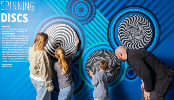 A family of four stand looking at an illusion on a wall.