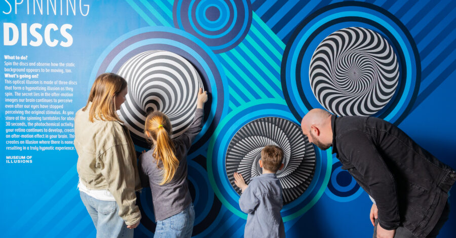 A family of four stand looking at an illusion on a wall.